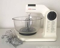 Sunbeam Mixmaster Model IM-95 stand mixer with glass bowl and three beater attachments placed beside it on white surface.