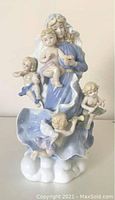 Front view of porcelain musical figurine showing the woman in blue holding a child surrounded by four cherubs with musical instruments