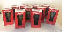 Set of 10 Coca-Cola green tinted drinking glasses in original red Coca-Cola boxes arranged together.