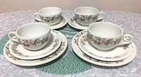 Photo showing 4 apple blossom patterned cups with matching saucers and dessert plates arranged on tablecloth.