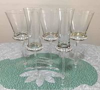 Five clear glass stemware glasses featuring diamond-like jewel decoration around the bowl base. Three are wine glasses and two are champagne flutes.