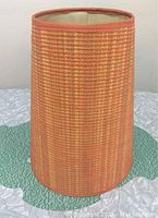Full external view of the orange textured fabric cone-shaped lamp shade on a quilted surface.