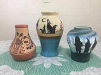 Photo showing three vases with varying shapes and painted designs on cloth surface