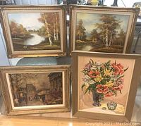 Four framed artworks displayed on floor: two autumn landscape oils, one Parisian street print, one floral acrylic print.