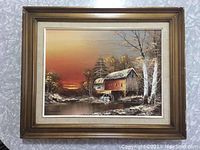 Full view of framed vintage oil on canvas painting showing a rustic watermill by a river at sunset.