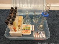 Full view of the science kit items arranged in a clear plastic bin including test tubes, beakers, and litmus paper
