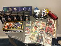 Collection showing hockey trading cards, pencil case box, helmets, and trophy miniatures arranged on table and floor.