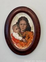Front view of the oval oil painting showing a woman holding a baby and the wooden frame with a crack on the top right.