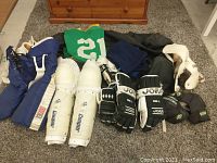 Top down view of various hockey protective equipment laid on the floor including CCM pants, Cooper shin pads, Jofa gloves, Koho gloves, Bauer elbow pads, hockey socks and jersey