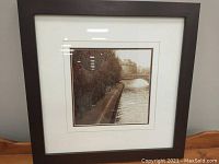 Front view of framed black and white photo of Paris Left Bank with dark brown wide wood frame and double layered white and gold matting.