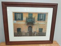 Framed photo of an orange building facade with green shutters and a balcony, showing the entire framed piece.
