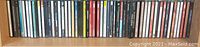Photo showing a lineup of approximately 30 music CDs on a shelf