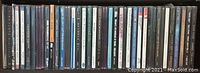 Photo of a collection of 25 music CDs lined up side by side showing their spines with artist and album titles.