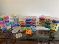 Thirty-four small plastic storage containers in various colors on a dark surface with colorful beads visible inside containers.