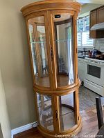 Curved wooden display cabinet with glass panels and mirrored back, shown standing in kitchen area.