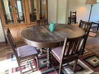 Full view of the antique dining table with six chairs placed around it, showing the dark wood finish and rounded rectangular shape.