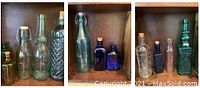 Twelve assorted glass bottles varying in size, color, and shape arranged in wooden shelving; includes clear, amber, cobalt blue and green bottles with a blue bottle containing white marbles.