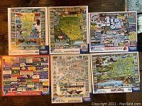 Six assembled puzzles laid out on wooden floor showing detailed regional US maps and highlights