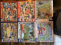 Five completed jigsaw puzzles box covers laid out showing the full collection titled Cape Cod, North Carolina, I Love Georgia, The State of Maine, United States Presidents, and I Love Minnesota.
