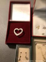 Heart-shaped pendant with rhinestones in red velvet-lined box along with other boxes containing earrings.
