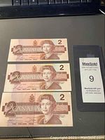 Three Canadian two dollar bills front side with Queen Elizabeth II portraits and denominations visible.