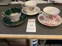Three tea cup and saucer sets displayed on a table, showing different floral patterns and colors.