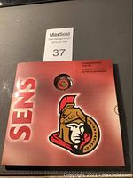 Front of the closed red folder featuring a large Ottawa Senators logo and the text 'SENS' and 'Commemorative Coin Set'