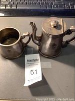 Two-piece pewter finished creamer and sugar set with maxsold lot ticket to identify the items.