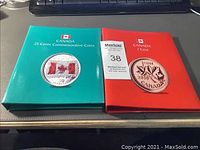 Two binders on a desk: green binder labeled '25 Cents Commemorative Coins' and red binder labeled '1 Cent', both Canada branded.