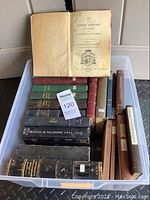 Photo of multiple old religious books in a plastic bin, showing worn covers, various sizes and colors including brown, black, green, and red.