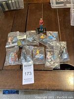 Overview of TinTin figurines on wooden surface, most sealed in plastic bags, one unbagged figurine on black base
