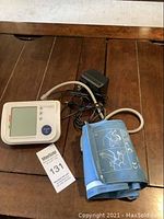 Digital blood pressure monitor with cuff and power adapter on wooden surface.