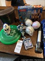 View of sports collectables including binoculars in leather case, box for Absolution training device, two baseballs (one in protective plastic), hockey goalie mask figurine, hockey player figurine, collectible hockey cards, and bike pump.