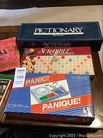 Board games Pictionary, Scrabble, and Panic! stacked on a table.
