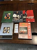 Five concert DVDs laid out on a wooden table. Visible titles include John Lennon & The Plastic Ono Band Live in Toronto '69, Paul McCartney In Red Square, The Beatles Songs That Changed The World including I Want To Hold Your Hand, and two DVDs related to The Beatles and John Lennon.