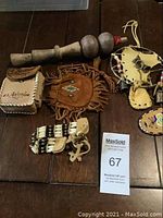 Photo showing a wooden mallet, various leather pouches with beadwork, a small carved wooden figure, and other leather and beaded indigenous items arranged on a table.