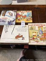 Four Calvin and Hobbes books by Bill Watterson arranged on a wooden surface showing full covers with graphic illustrations.