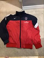 Front view of the men's XL spring jacket in red and black, showing the Nike swoosh on right chest, Paris Saint-Germain logo on left chest, and Fly Emirates embroidered sponsorship on front.