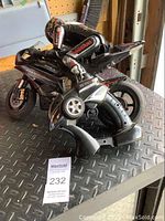 Side and top view of the black Winyea remote control motorcycle with the rider figurine positioned on top. The motorcycle has racing decals and detailed wheels. The remote control is positioned upright next to the motorcycle.