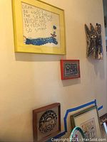 Framed child's drawing with visible water stain, accompanied by three other artworks on the wall nearby