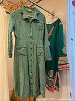 Full view of the vintage greenish long-sleeve dress with button front and two patch pockets. Ethnic embroidered patches visible on sleeves and hem.