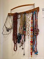 Wooden jewelry wall hanging with various colorful necklaces and earrings hanging on it.