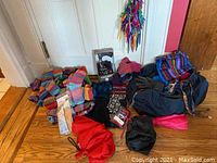Full overview of lot with gloves, socks, colorful scarves, umbrellas, bags, and knit hat arranged on hardwood floor in front of a white door.