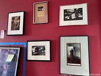 Five framed photographs on a red wall featuring portraits and abstract scenes. Two photographs are signed.