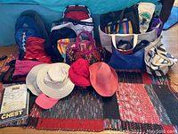 Overall view of all bags and hats laid out on a rug showing backpacks, totes, handbags and hats