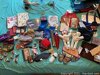 Wide shot of lot items spread on bed including purses, bibs, socks, cutting board, voodoo doll napkin rings, and assorted novelty items.