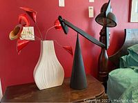 Full view of lamp and vase with faux flowers on tabletop against red wall
