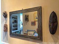 Full view of large ornate metal framed mirror with three wooden masks on wall around it