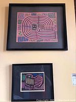 Two framed textile wall art pieces hung on a wall, one above the other, with black frames and black matting.