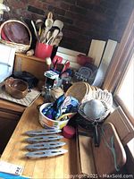 Overall view of kitchen countertop with cast iron skillets, wooden utensils, and various containers and baskets collecting small kitchen items.